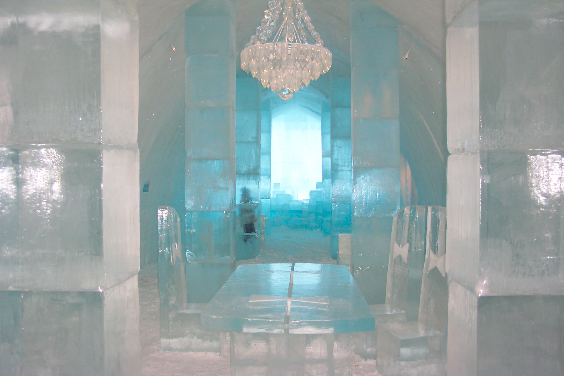 Distance shot of the chandelier at the ice hotel with Thomas' son in the background against a window which shines blue in the light. 