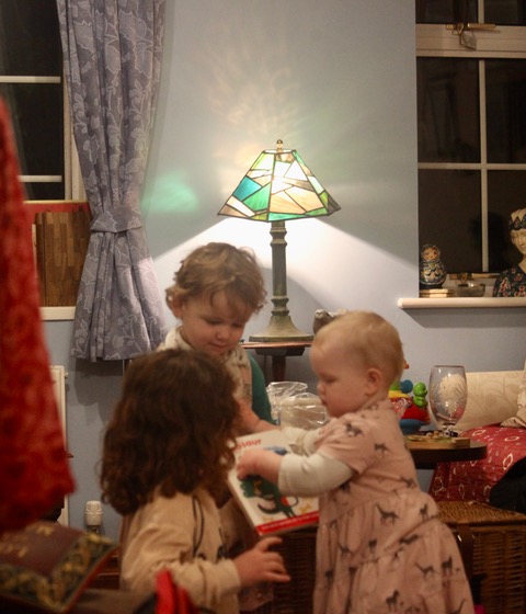 Three children playing with a chandelier in the background made from coloured pieces of glass. 