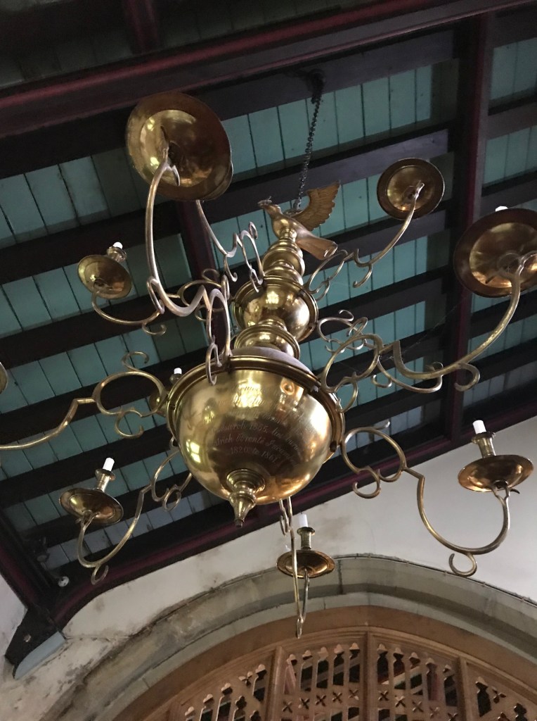 Close up of the brass chandelier dedicated to the Bronte family. It has a large semi circular brass centrepiece with the Bronte family dedication etched onto it and several smaller brass lights shaped liked old fashioned candleholders. 