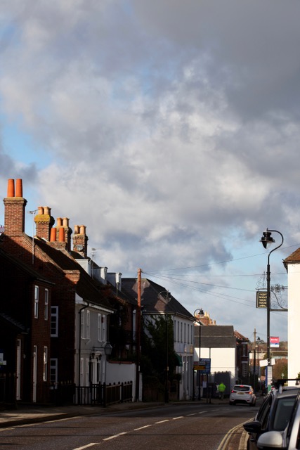 A street with a row of houses with chimneys and a fancy streetlight. 