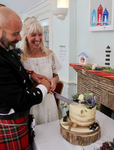 a gorgeous picture of Barry and Karen cutting their wedding cake which has two tiers and its toped with purple and white flowers. 