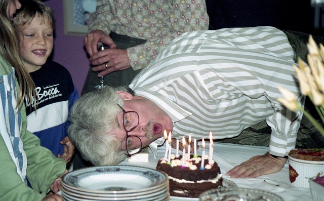 Photograph of Derrick Knight leaning right over to blow out the candles on his 50th birthday cake.