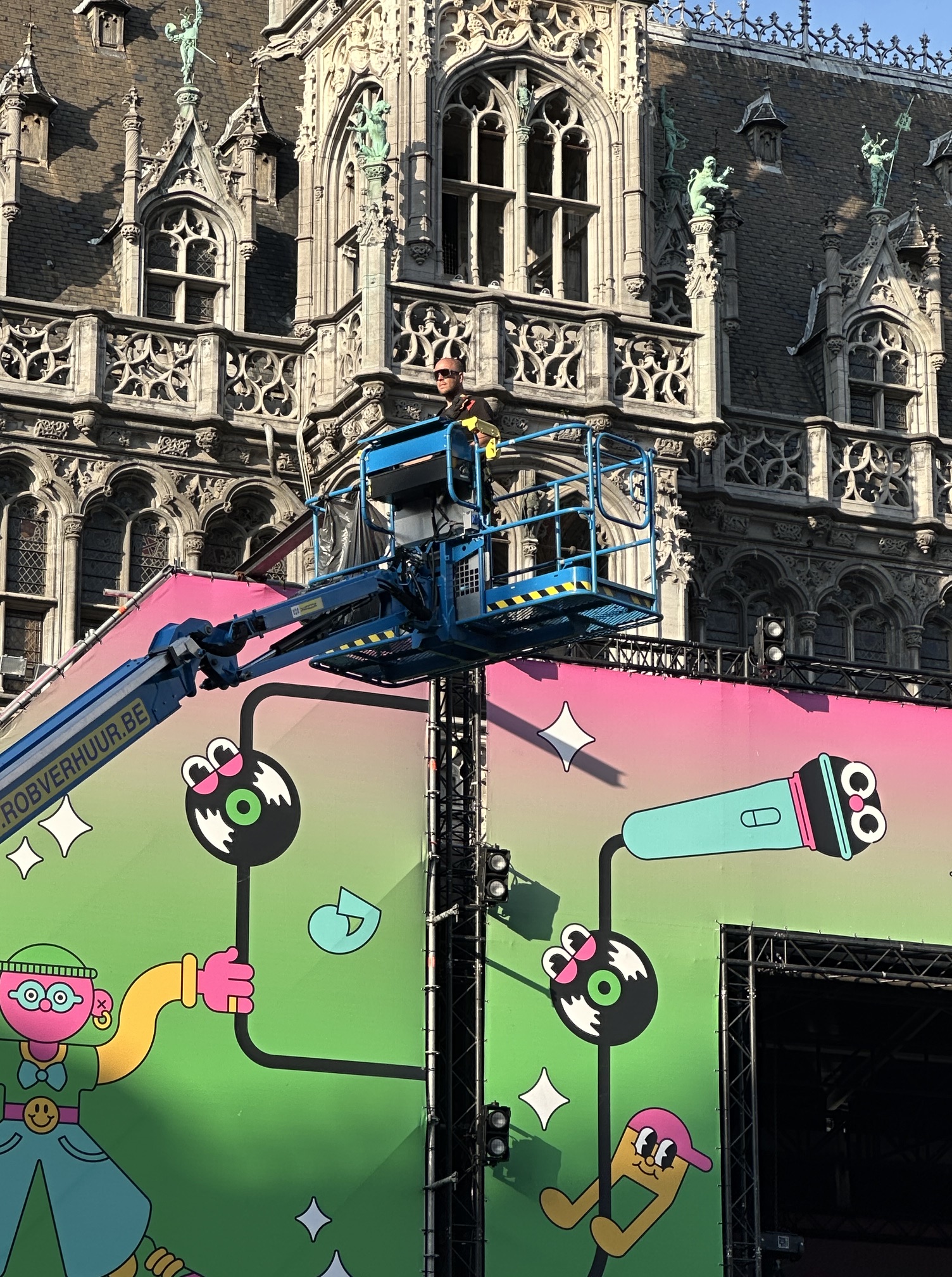 Another machine with a fenced platform. On it stands a man who is directing the construction of a stage for a music concert in Brussels.
