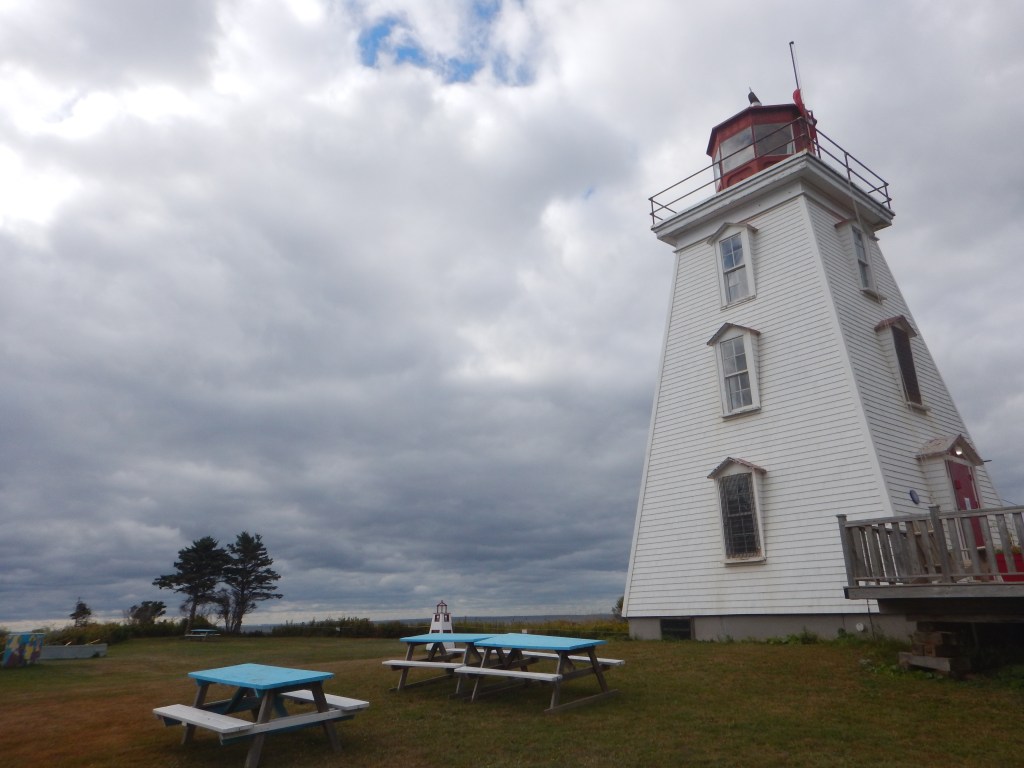 A close up of the lighthouse mainly from the front with picnic tables in front of it. 